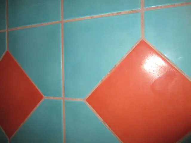 A wall with a geometric tile pattern features turquoise squares, each bordered with thin grout lines, and orange diamond shapes interspersed between them. An investigation into the design reveals a sampling of colors that create striking contrasts.