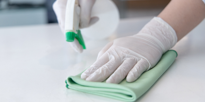 A person wearing white gloves conducts an assessment while cleaning a surface with a green cloth and a spray bottle, ensuring no mold is present.
