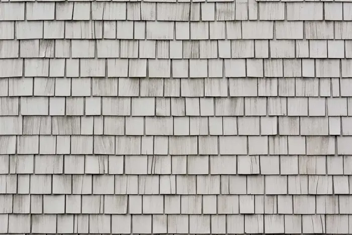 Close-up of a wall covered with overlapping rectangular wooden shingles, arranged in a uniform pattern. Upon inspection, the weathered shingles reveal variations in color from light gray to dark gray, creating a textured appearance.