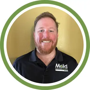 Smiling man with short reddish hair and beard wearing a black polo shirt with a Mold Inspection Sciences Texas logo, standing in front of a yellow wall, framed by a green and white circular border—ready for mold investigation.