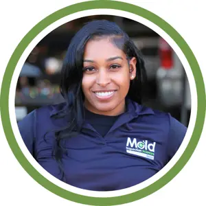 A woman with long black hair, smiling, wears a navy blue Mold Inspection Sciences Texas shirt. She is framed by a green and white circular border, representing the company’s commitment to thorough inspection. The background is blurred.